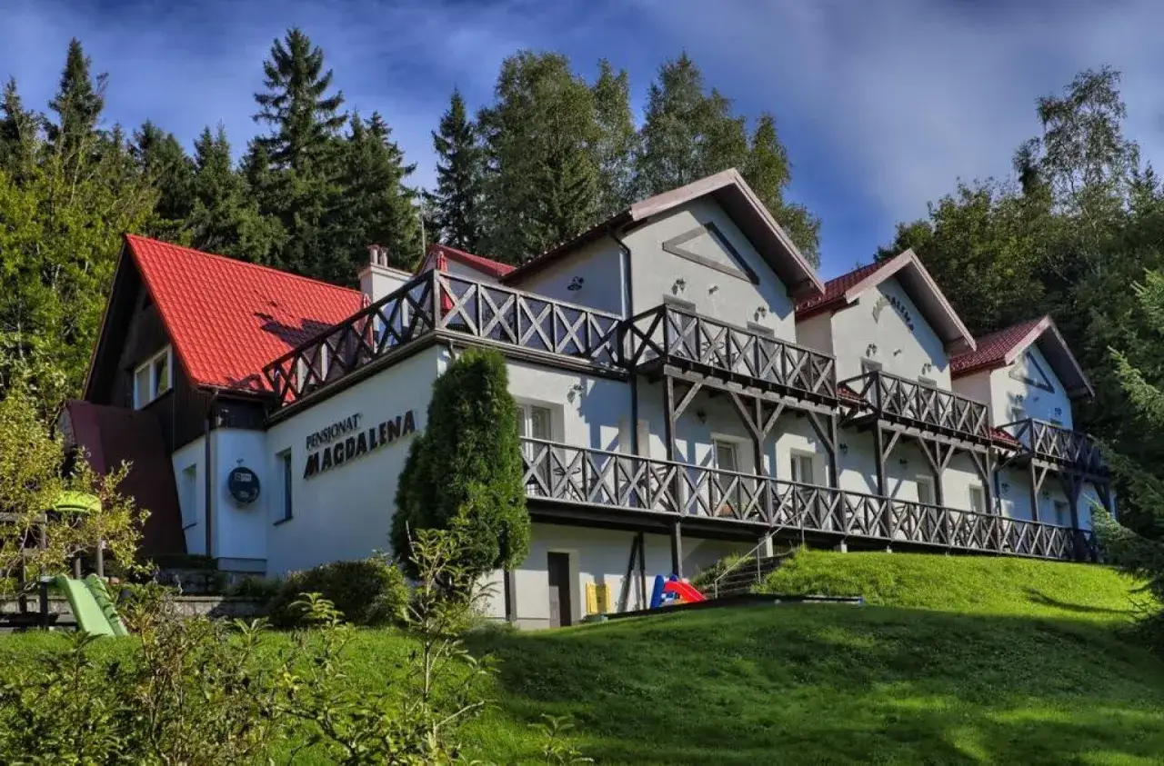 Pensjonat Magdalena z czerwonym dachem, otoczony zielenią i lasem.