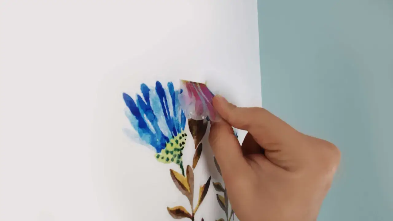 Dłoń przykleja naklejkę z kwiatem. Aby naklejka się nie odklejała, upewnij się, że powierzchnia jest czysta i sucha.