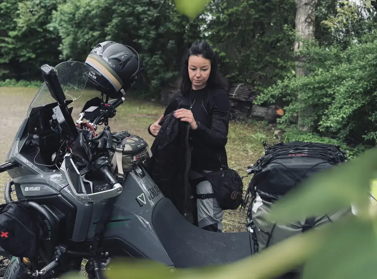 Kobieta pakuje plecak na motocykl. Zastanawia się, co zabrać na wyprawę motocyklową, by niczego nie zapomnieć.