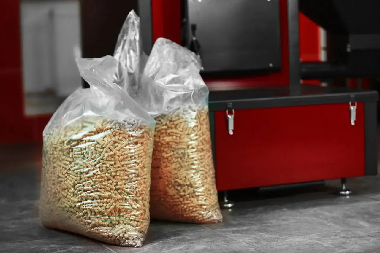 Dwa worki z pelletem drzewnym na tle czerwonego kotła na pellet.