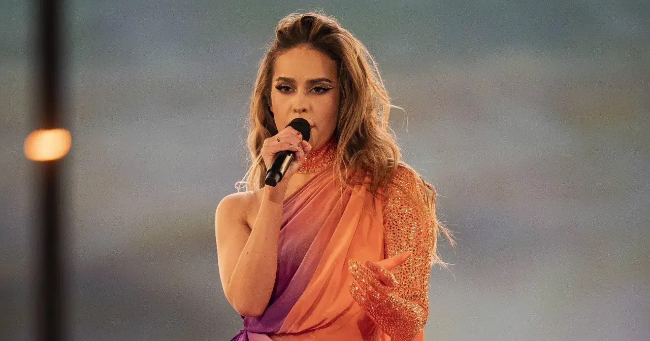 Kto śpiewa piosenkę solo solo? Młoda artystka w pomarańczowo-fioletowej sukni z cekinami, z mikrofonem w dłoni, na tle rozmytego światła.