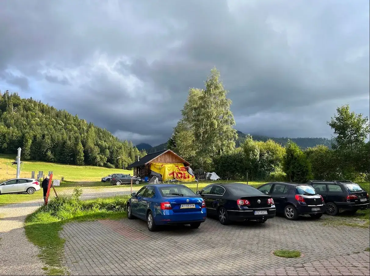 Kasprowy Wierch parking pod burzowym niebem. Kilka samochodów zaparkowanych przy górskiej chatce z żółtym banerem.
