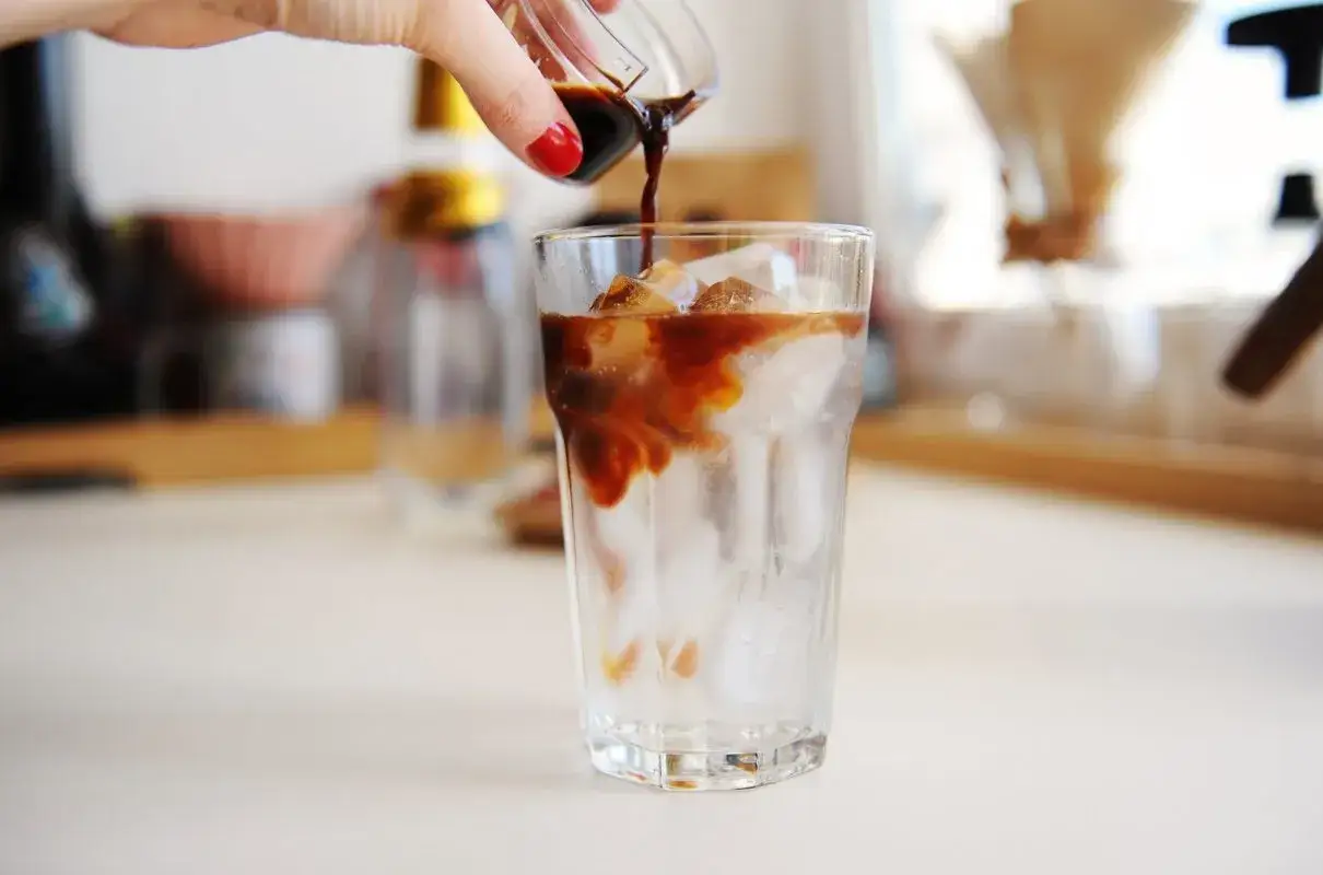 Ręka wylewa espresso na lód w szklance. Idealny napój na upalne dni - tonic espresso.