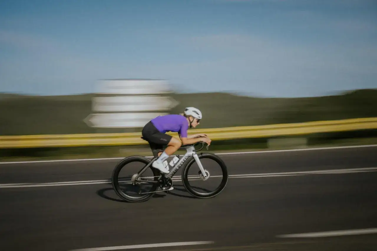 Kolarz w fioletowej koszulce pędzi na rowerze, osiągając prędkość 50 km/h.