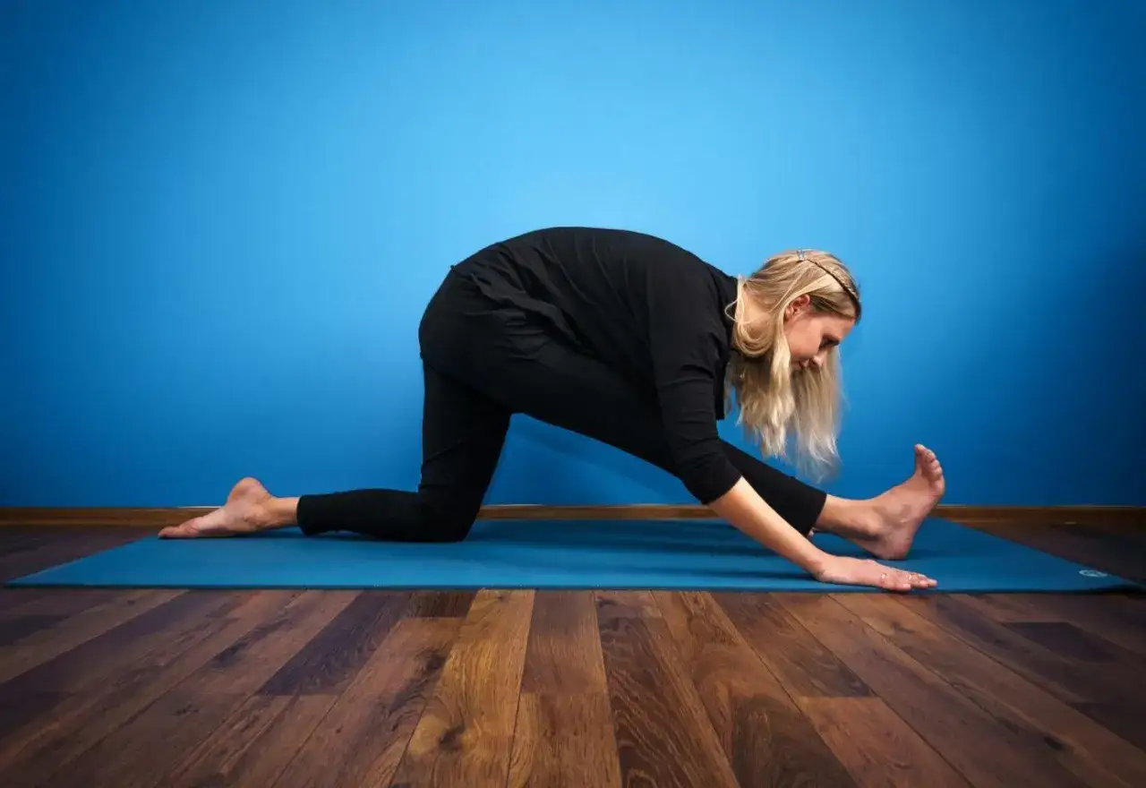 Kobieta w czarnym stroju ćwiczy rozciąganie na macie, pochylając się do przodu.
