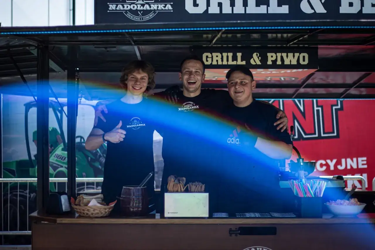 Trzech uśmiechniętych mężczyzn za ladą cateringową z napisem "Grill & Piwo".