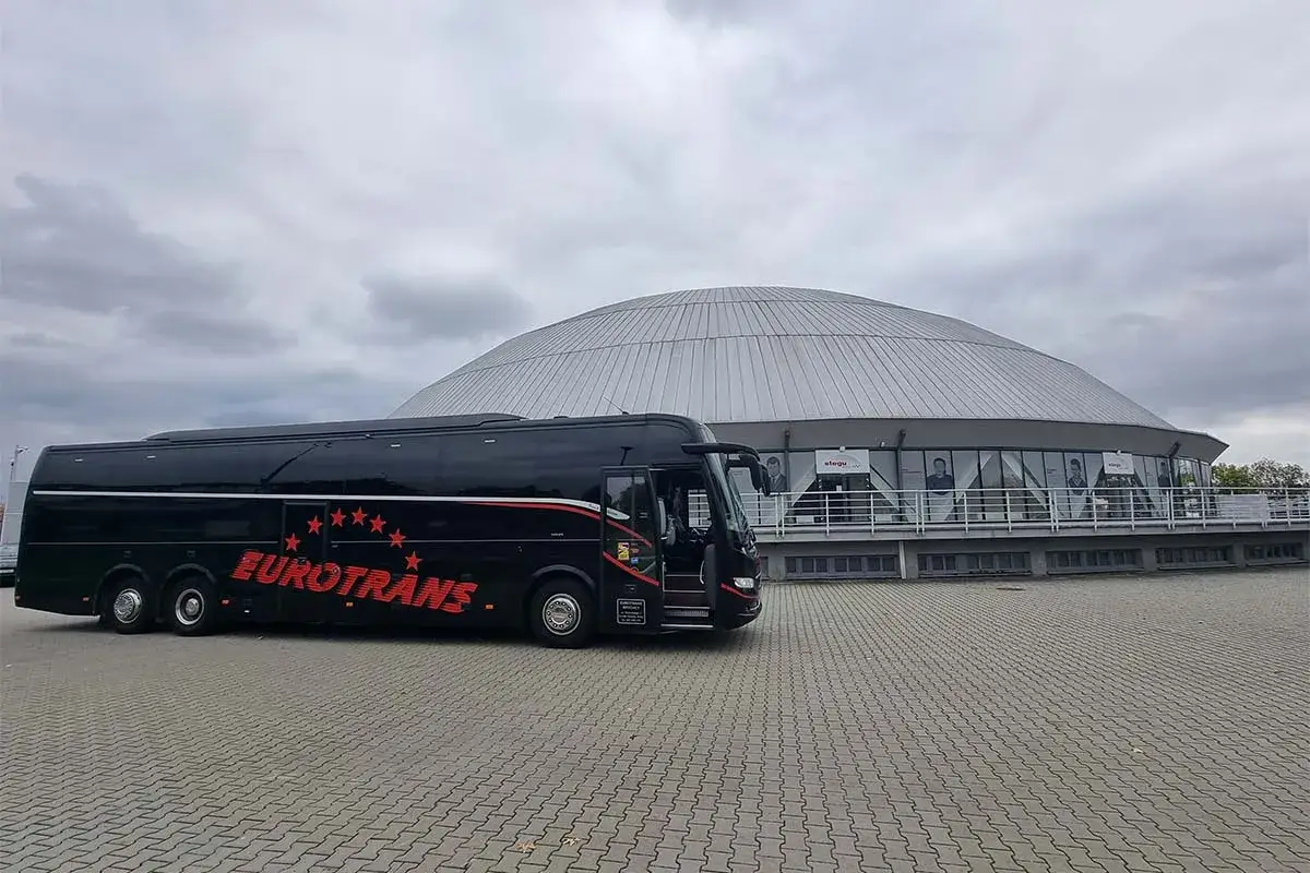 Czarny autokar turystyczny "Eurotrans" przed nowoczesnym budynkiem z kopułą.