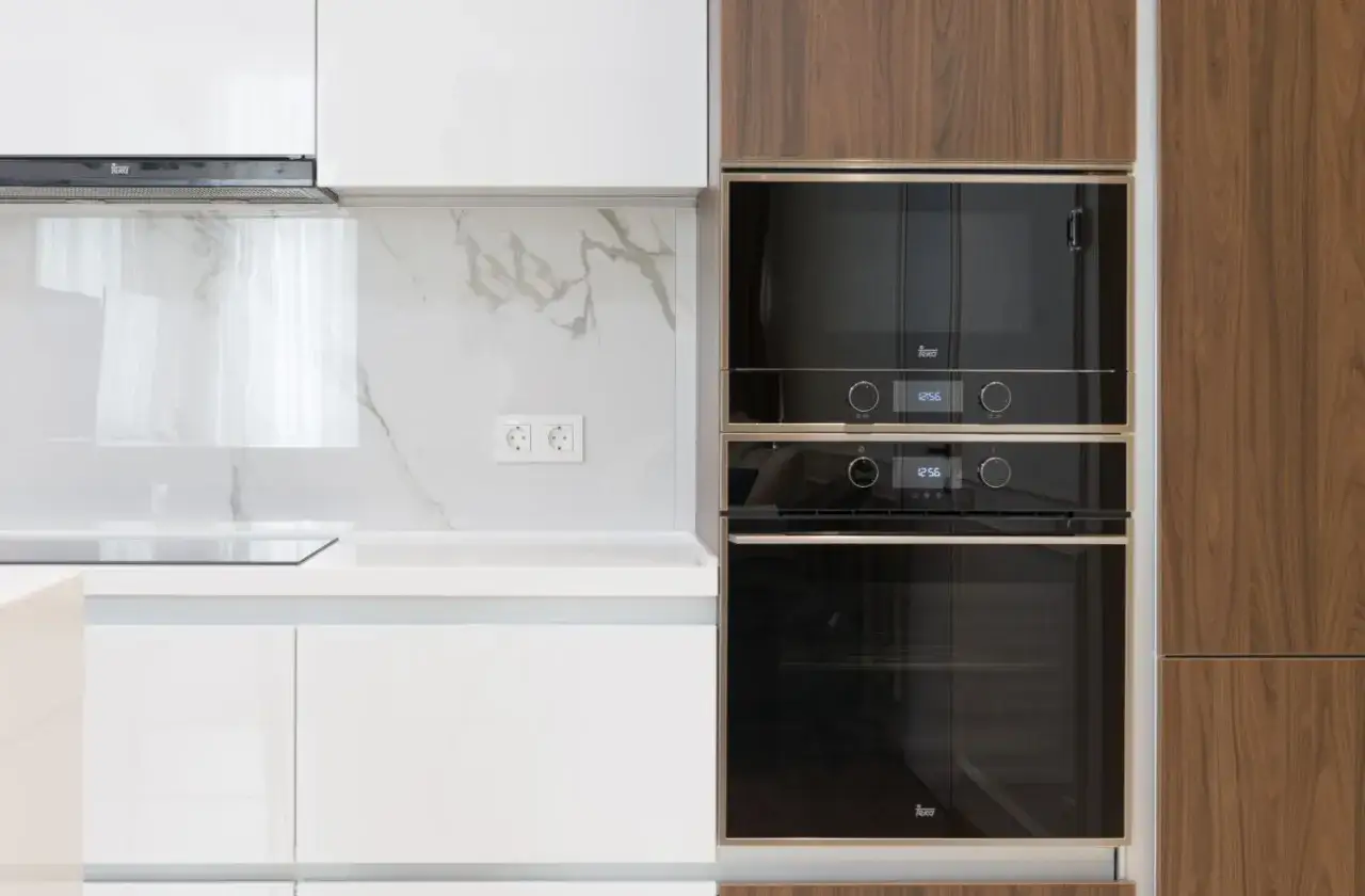 Nowe piekarniki w zabudowie. Jak wymontować piekarnik z zabudowy? Elegancka kuchnia z drewnianymi frontami i białymi szafkami.