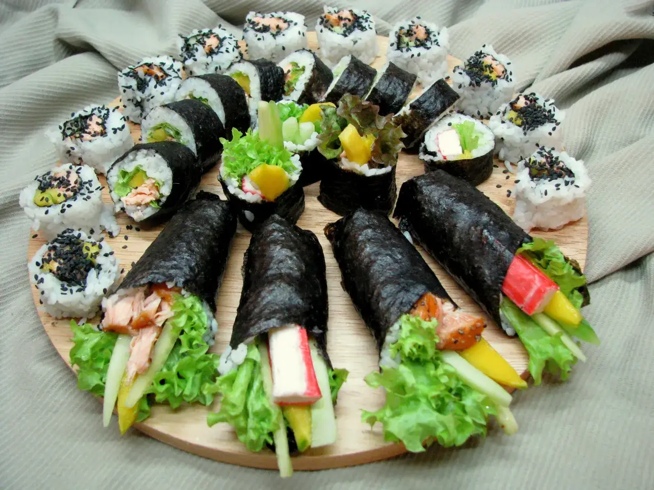 Talerz sushi z futomaki i uramaki. Widać rolki z łososiem, awokado, sałatą, paluszkami krabowymi i mango.