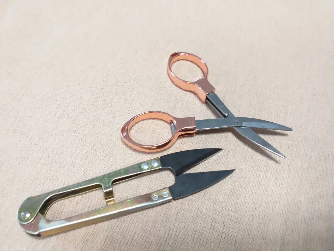 Dwa rodzaje nożyczek, w tym małe nożyczki z miedzianymi uchwytami i większe, metalowe, to niezbędne narzędzia i przybory krawieckie do precyzyjnych cięć.