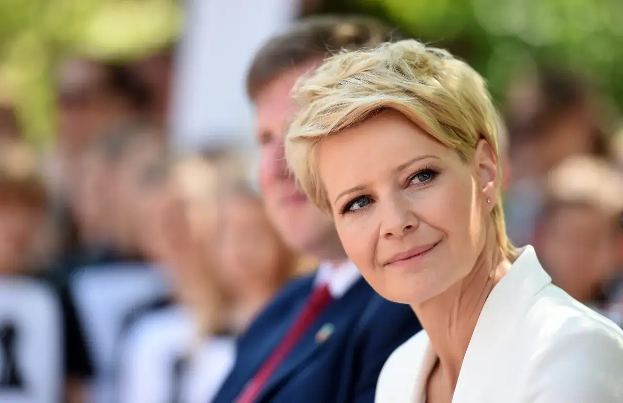 Kobieta z blond włosami w super krótkiej fryzurze damskiej, w białej marynarce, uśmiecha się.