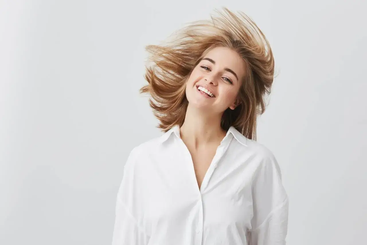 Uśmiechnięta dziewczyna z burzą blond włosów, które falują jak suche puszące się włosy.