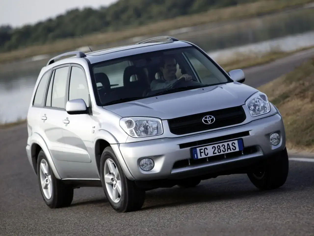 Srebrny SUV Toyota RAV4 na drodze, z kierowcą za kierownicą.