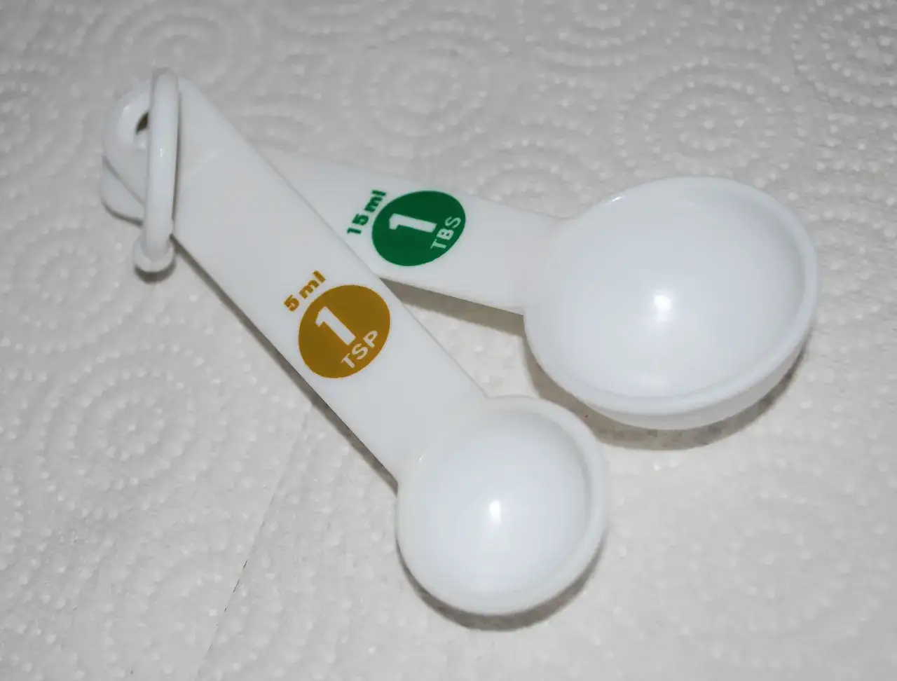 Dwie białe łyżki miarowe. Jedna ma oznaczenie 5 ml (1 TSP), druga 15 ml (1 TBS).