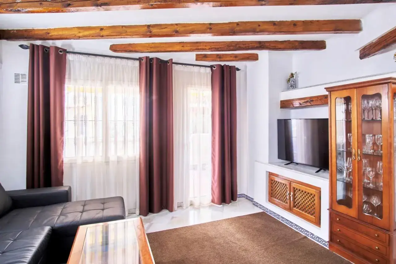 Salon z drewnianymi belkami na suficie, czarną kanapą i przeszkloną witryną. Zastanawiasz się, ile kosztuje wynajęcie mieszkania w Hiszpanii?