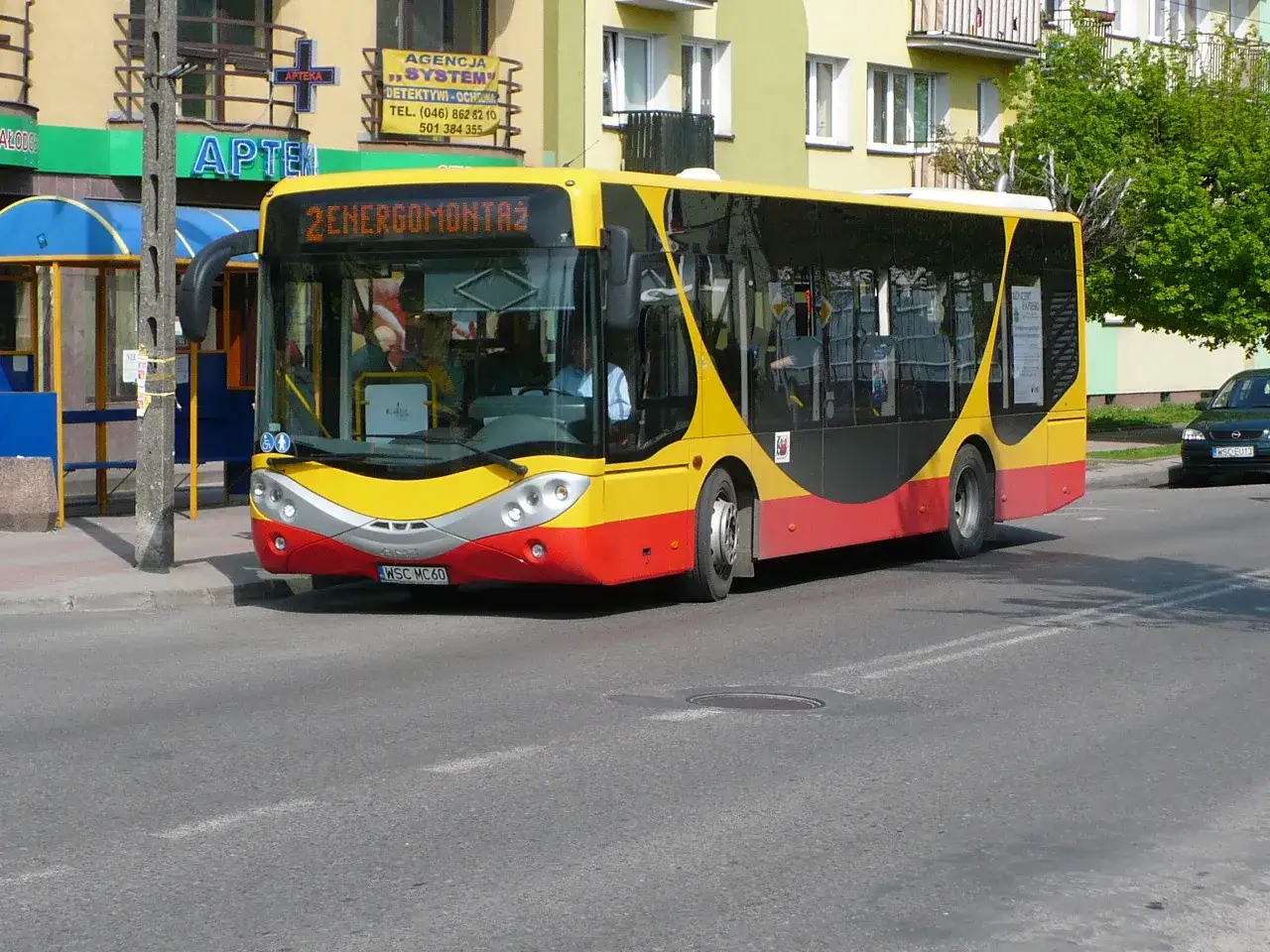 Żółto-czerwony autobus miejski z napisem "2 ENERGOMONTAŻ" na trasie w Sochaczewie.