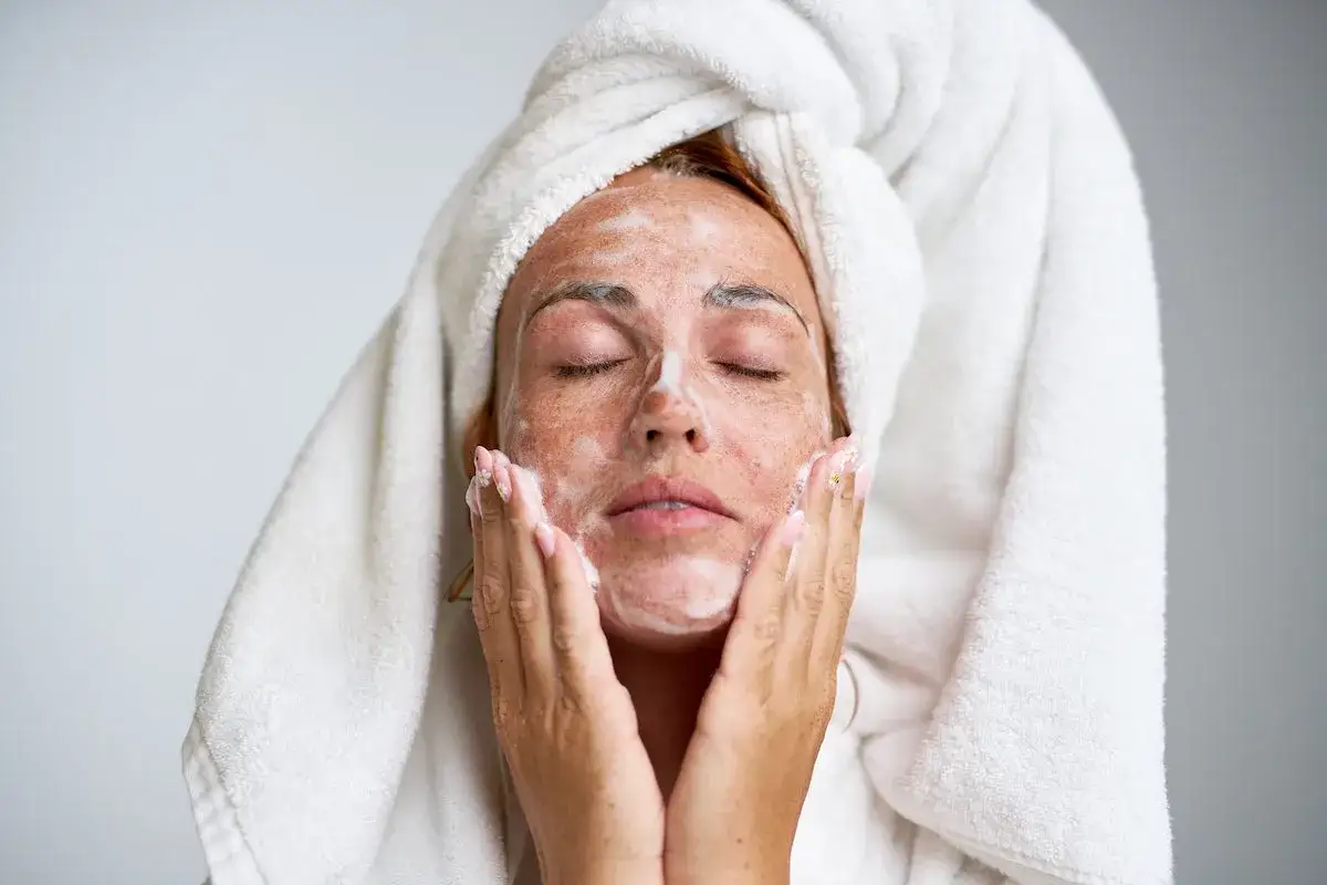 Kobieta z ręcznikiem na głowie myje twarz pianką.