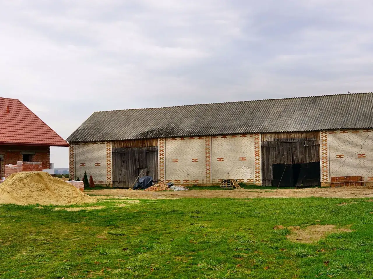 Dwa budynki gospodarcze, jeden z czerwoną, drugi z szarą, falistą papą na dachu. Obok sterta piasku i materiałów budowlanych. Czy garaż jest budynkiem według prawa budowlanego?