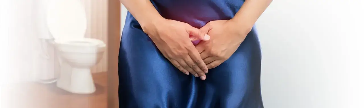 Kobieta w granatowej sukience z rękami na podbrzuszu, w tle toaleta. Problem z nietrzymaniem moczu? Czas na wizytę u lekarza.