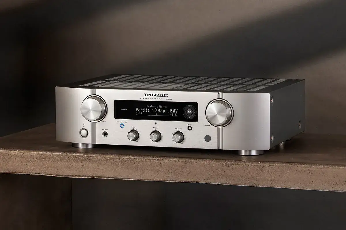 Srebrny wzmacniacz Marantz PM7000N, gotowy do testu, z wyświetlaczem pokazującym utwór muzyczny.