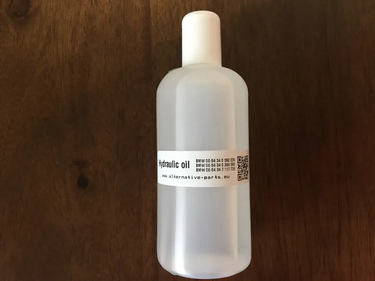 Biała butelka z olejem hydraulicznym na drewnianym tle.