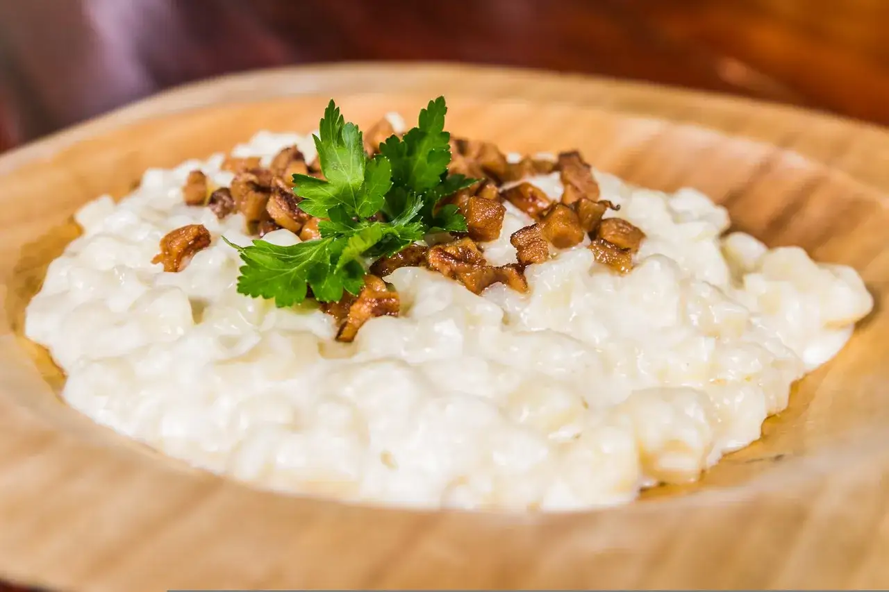 Bryndzové halušky z posypkou ze škvarků a petrželkou na dřevěném talíři.