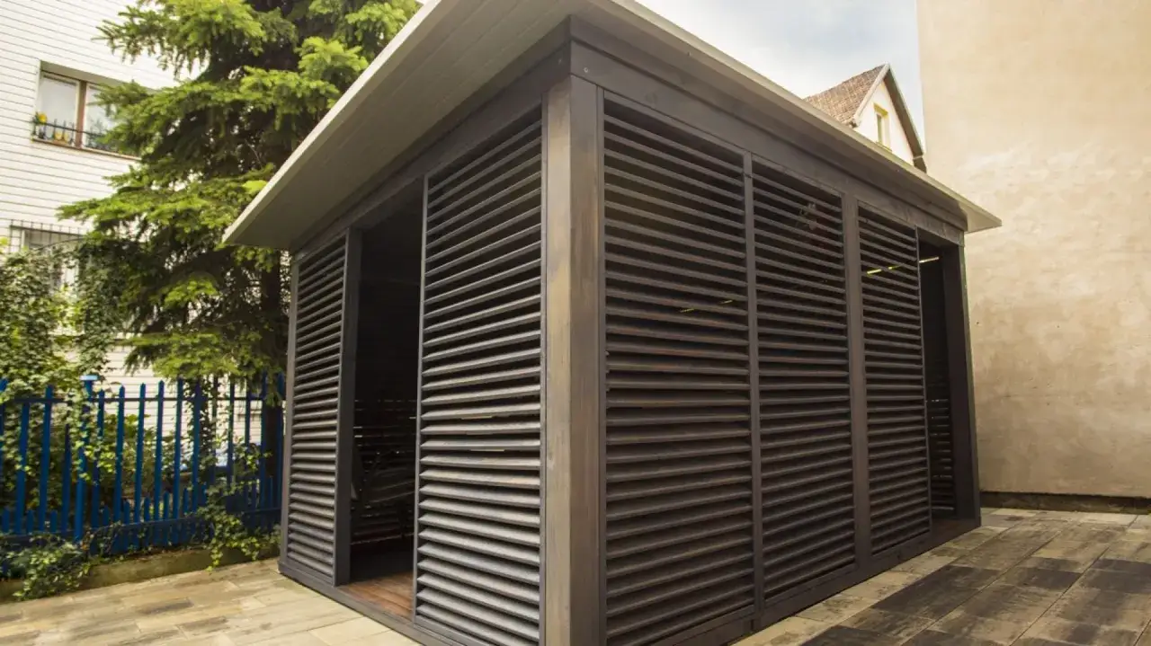 Ciemna altana z żaluzjami, idealna do ogrodu. Zastanawiasz się, czym pomalować altanę drewnianą? Ta prezentuje się świetnie!