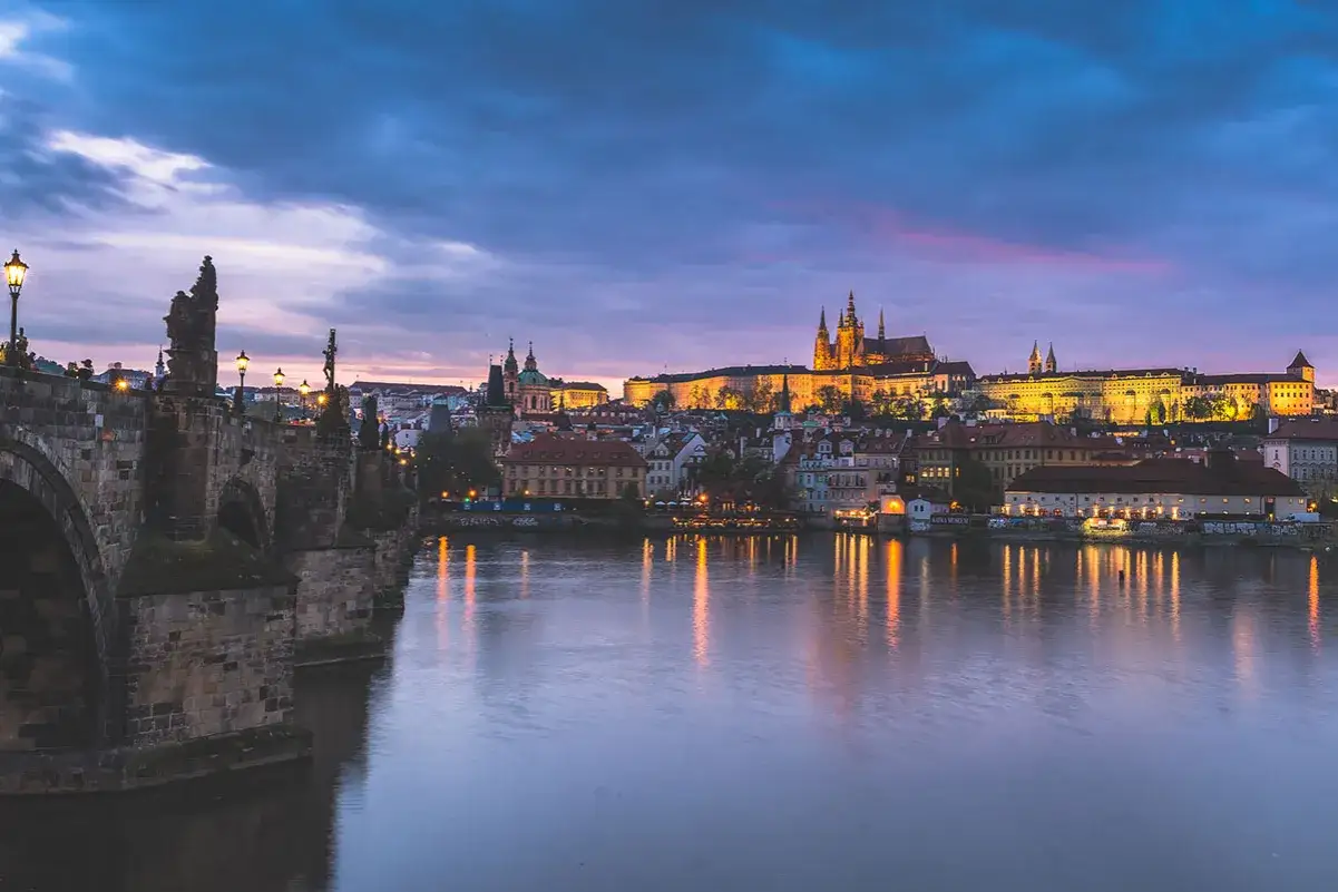 Nastrojowa fotografia nocna Pragi: Most Karola i Zamek na Hradczanach w blasku świateł, odbijających się w Wełtawie.