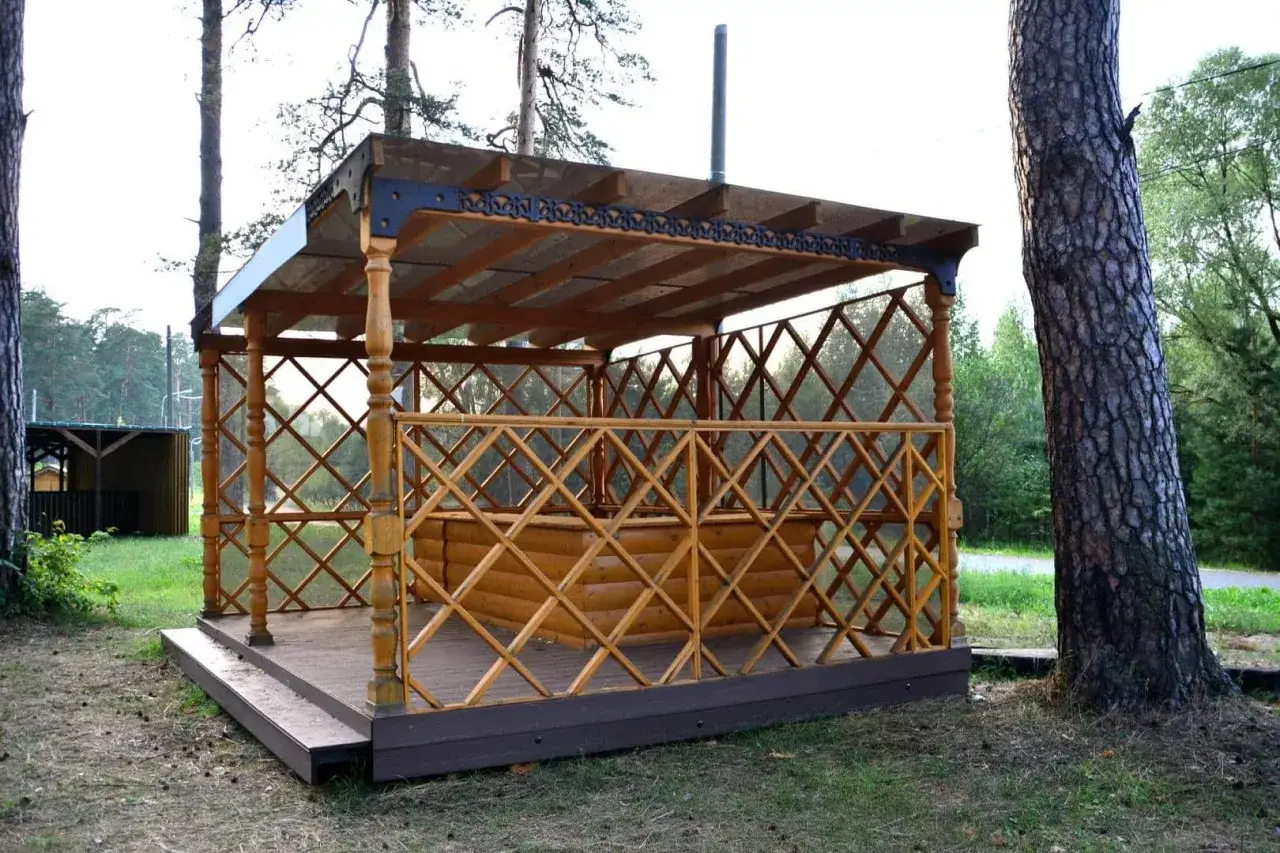 Drewniana altana z ażurową balustradą i przeszklonym dachem, stojąca na tarasie.