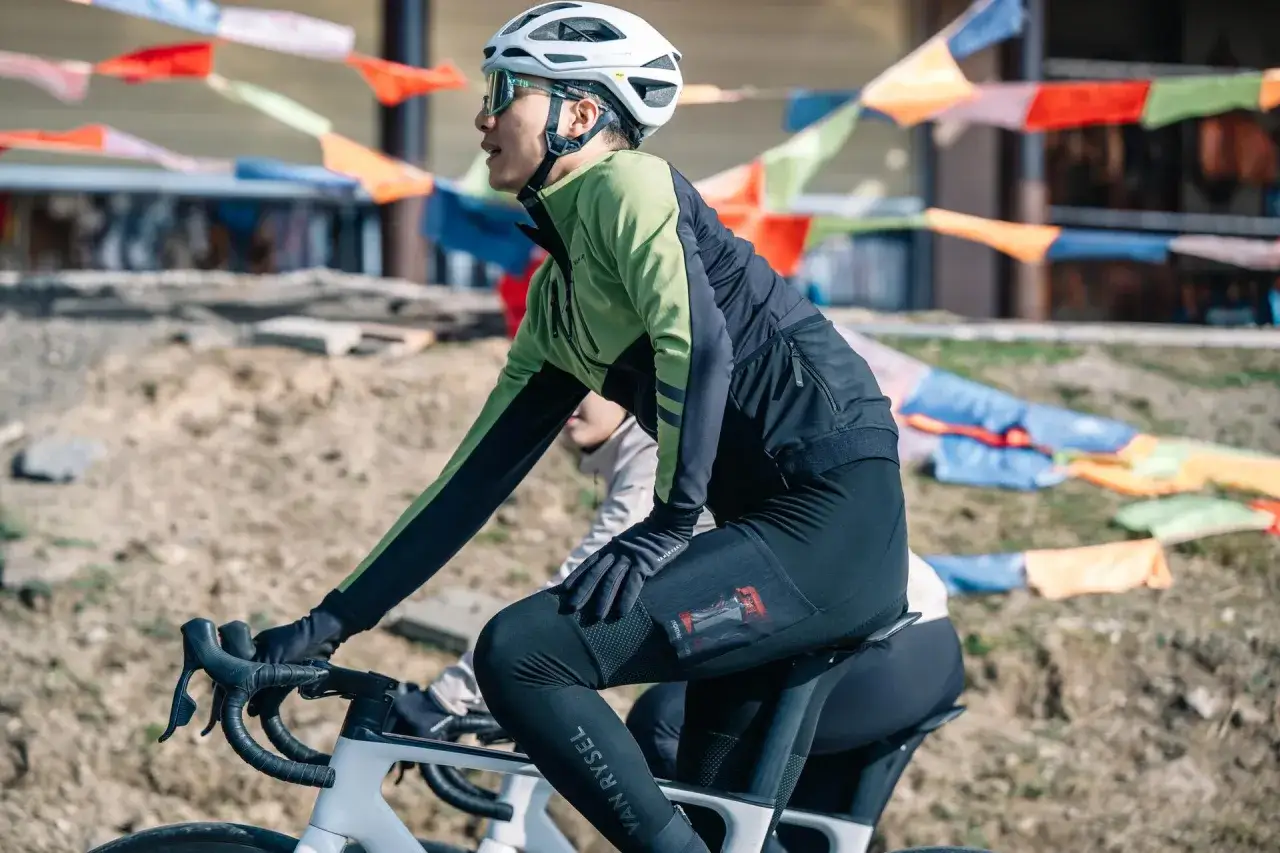 Kolarz w zielono-czarnej kurtce i czarnych spodenkach z kieszonką na żel energetyczny. To kluczowy element diety kolarza.