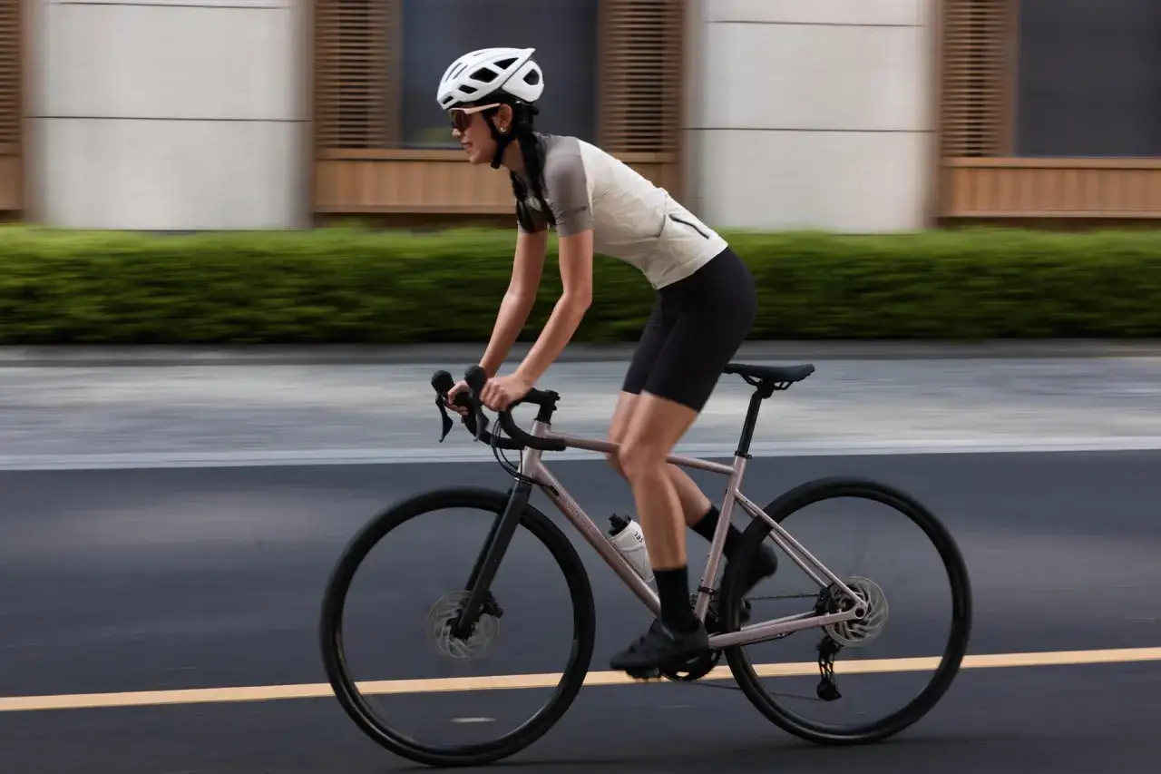 Kobieta w kasku i okularach jedzie rowerem. Długość korby a wzrost to klucz do komfortowej jazdy.