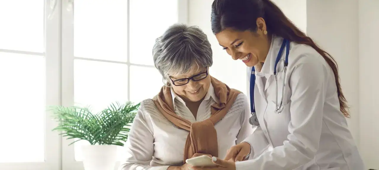 Uśmiechnięta lekarka pokazuje coś na telefonie pacjentce w sanatorium Iwonicz Zdrój.