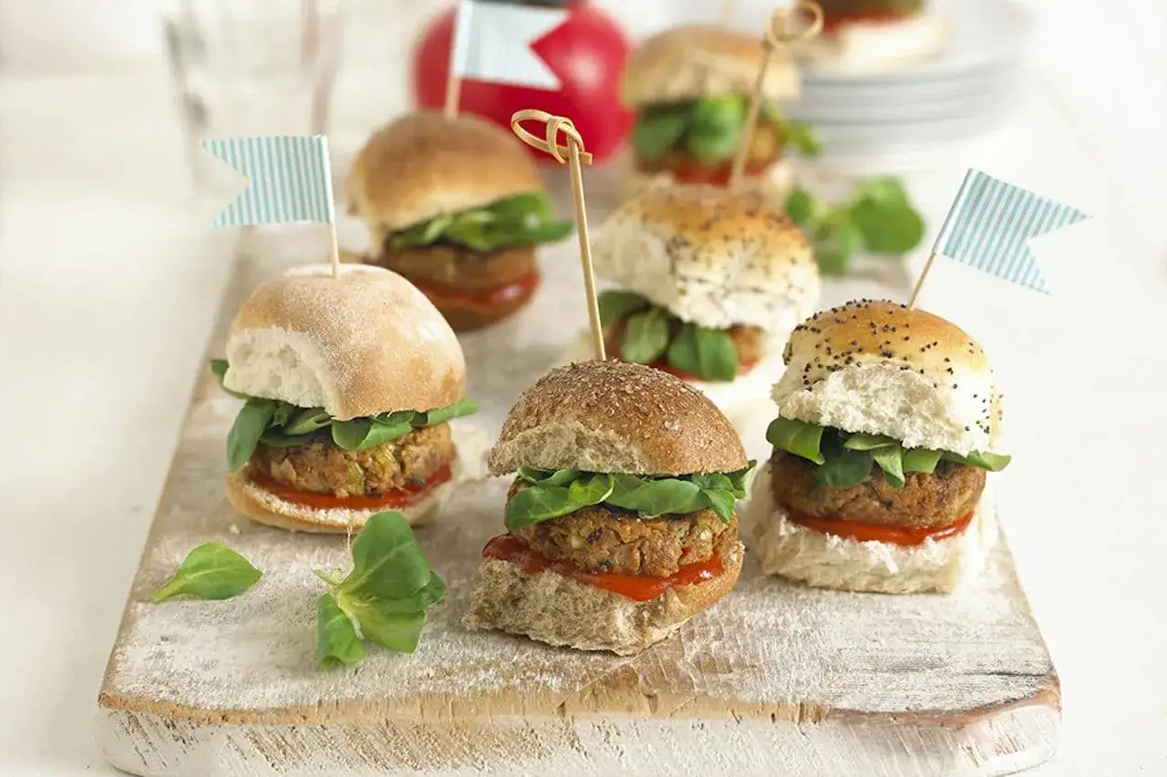 Mini bułeczki do hamburgerów z kotletami, sałatą i flagami na drewnianej desce.