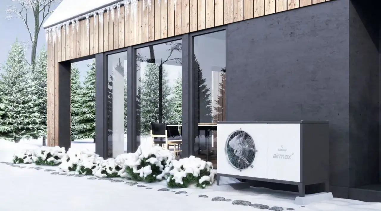 Nowoczesny dom w zimowej scenerii. Obok budynku stoi biała jednostka, która może być alternatywą dla pompy ciepła.