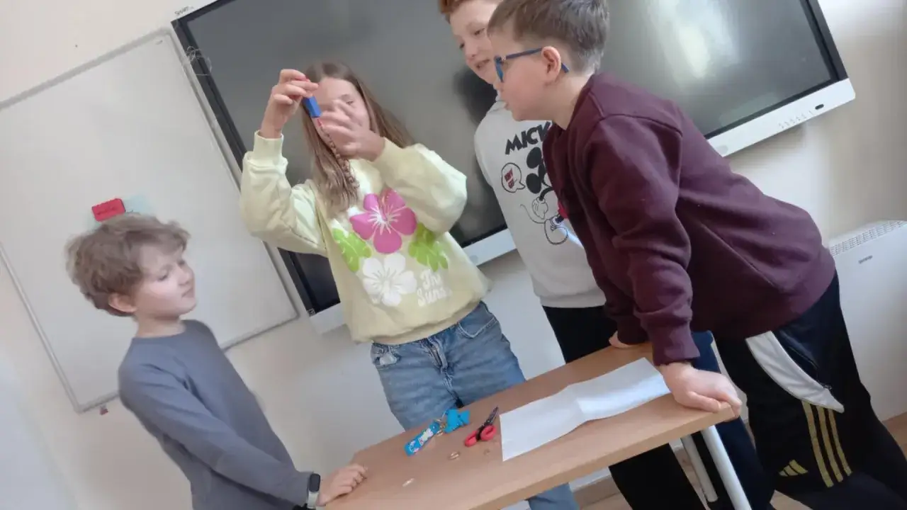 Dzieci przeprowadzają eksperyment z magnesem, trzymając go nad łańcuszkiem.