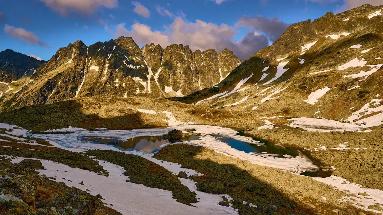 Góry Słowacji budzą się do życia, kiedy otwierają szlaki. Topniejący lód na jeziorze, skaliste zbocza i pierwsze promienie słońca.