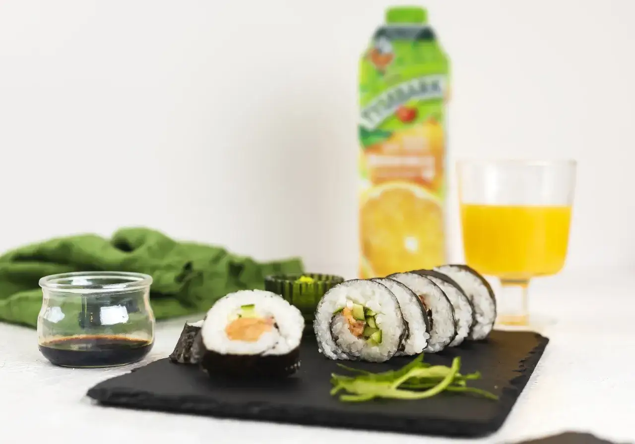 Pyszne sushi z łososiem, ogórkiem i ryżem, podane z sosem sojowym i sokiem pomarańczowym.