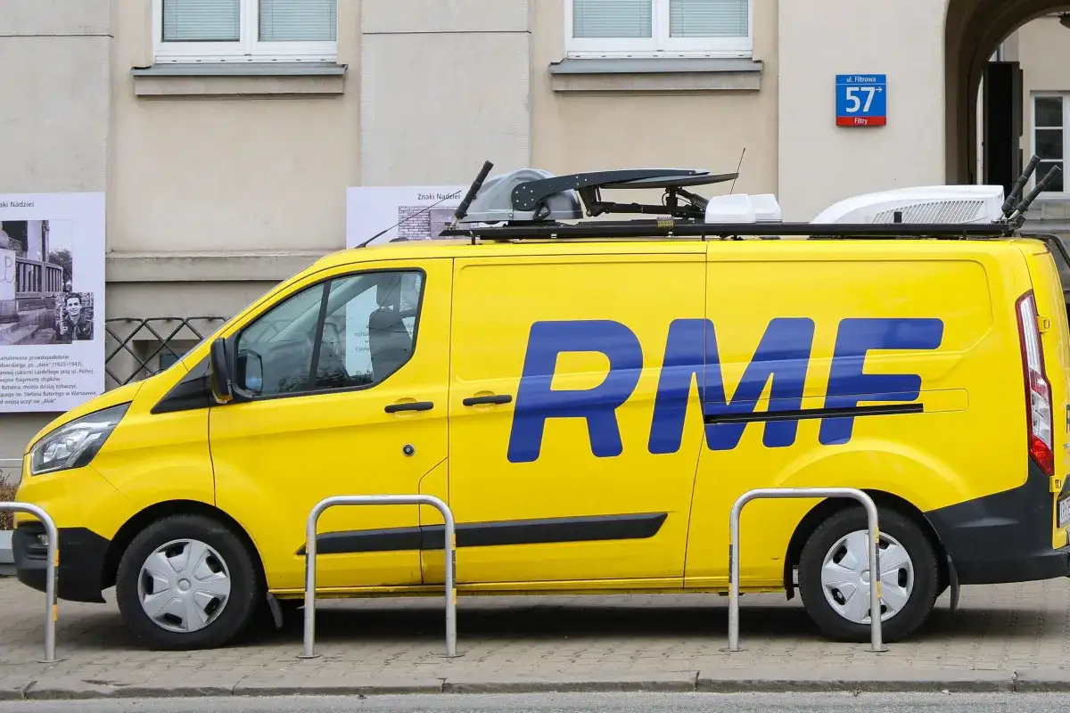 Żółty van RMF FM z niebieskim logo na tle budynku.
