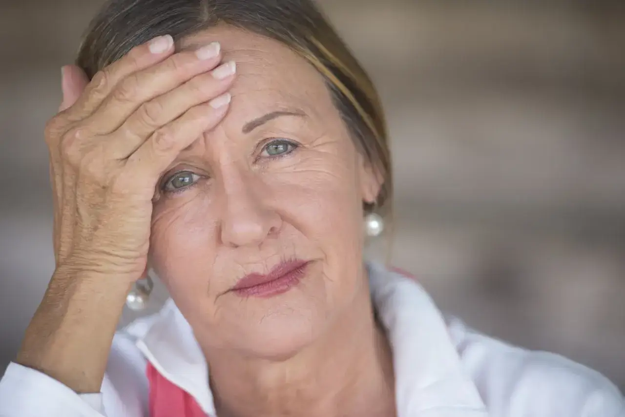 Zmartwiona kobieta z ręką na czole, szukająca ulgi w objawach menopauzy.
