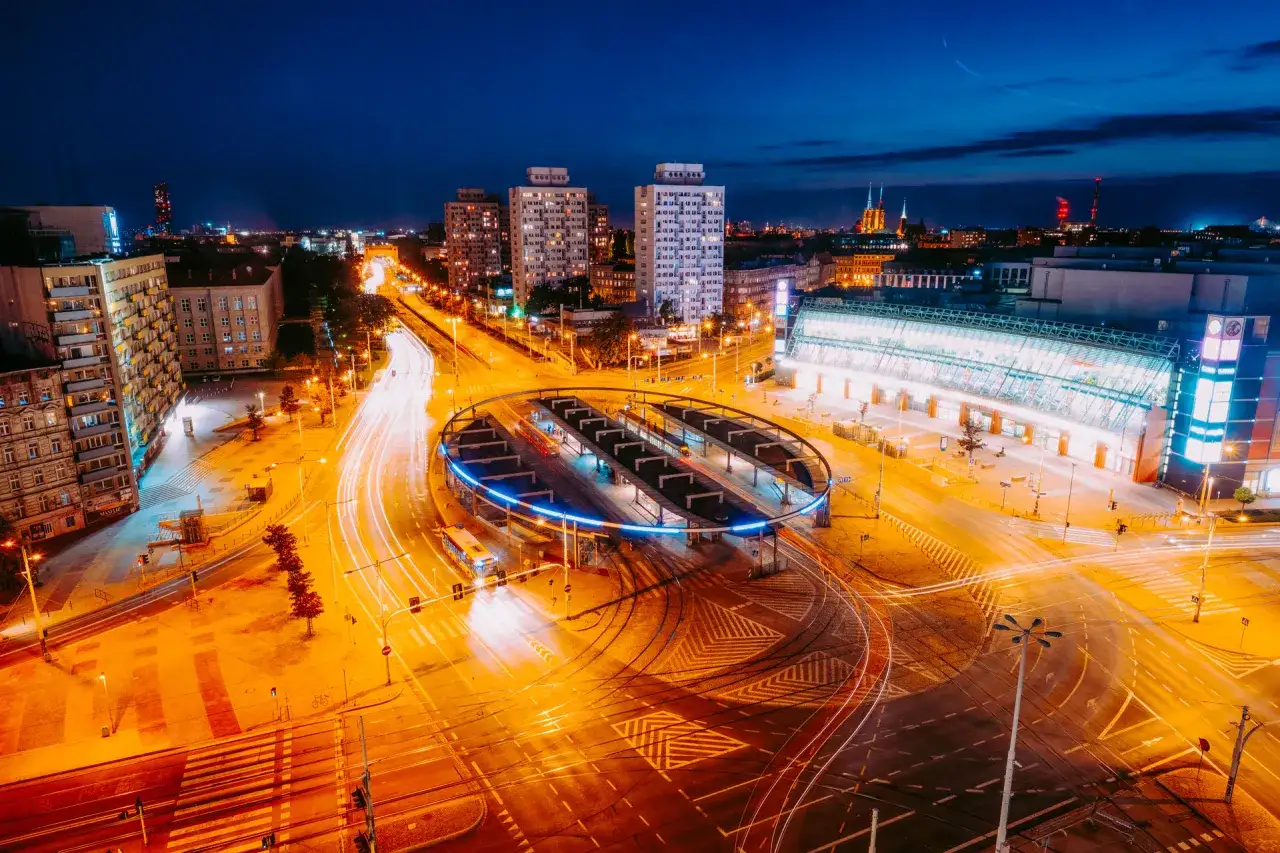 Widok z lotu ptaka na nocne miasto z długimi smugami świateł samochodowych i tramwajowych.