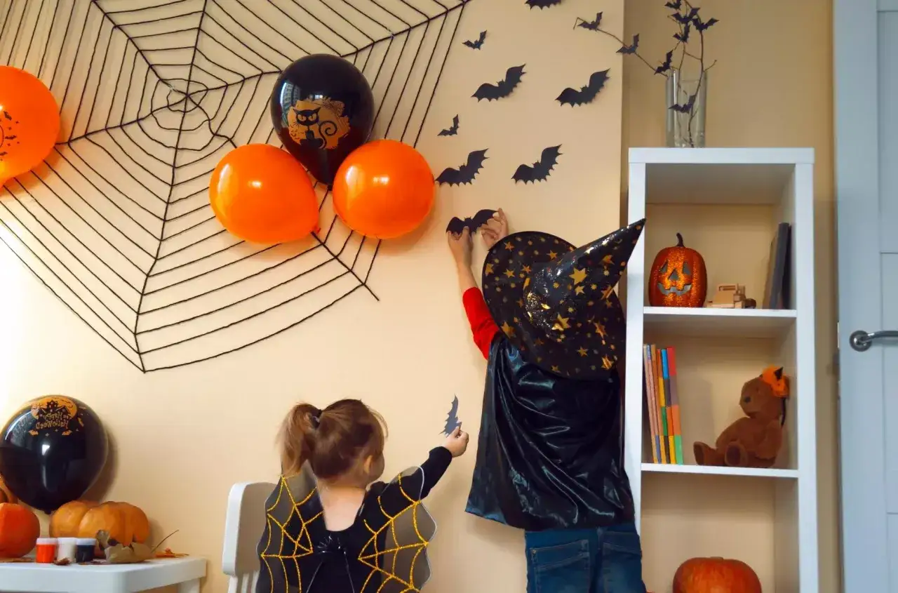 Dzieci w strojach na Halloween dekorują pokój, wieszając nietoperze na ścianie z wielką pajęczyną.