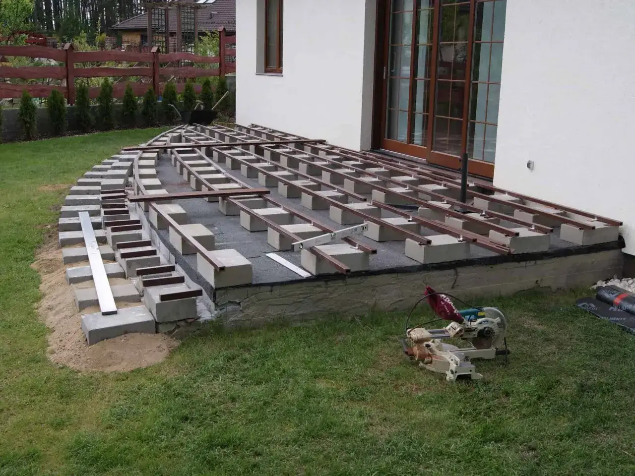 Budowa tarasu: betonowe bloczki i drewniane legary tworzą konstrukcję pod deski.