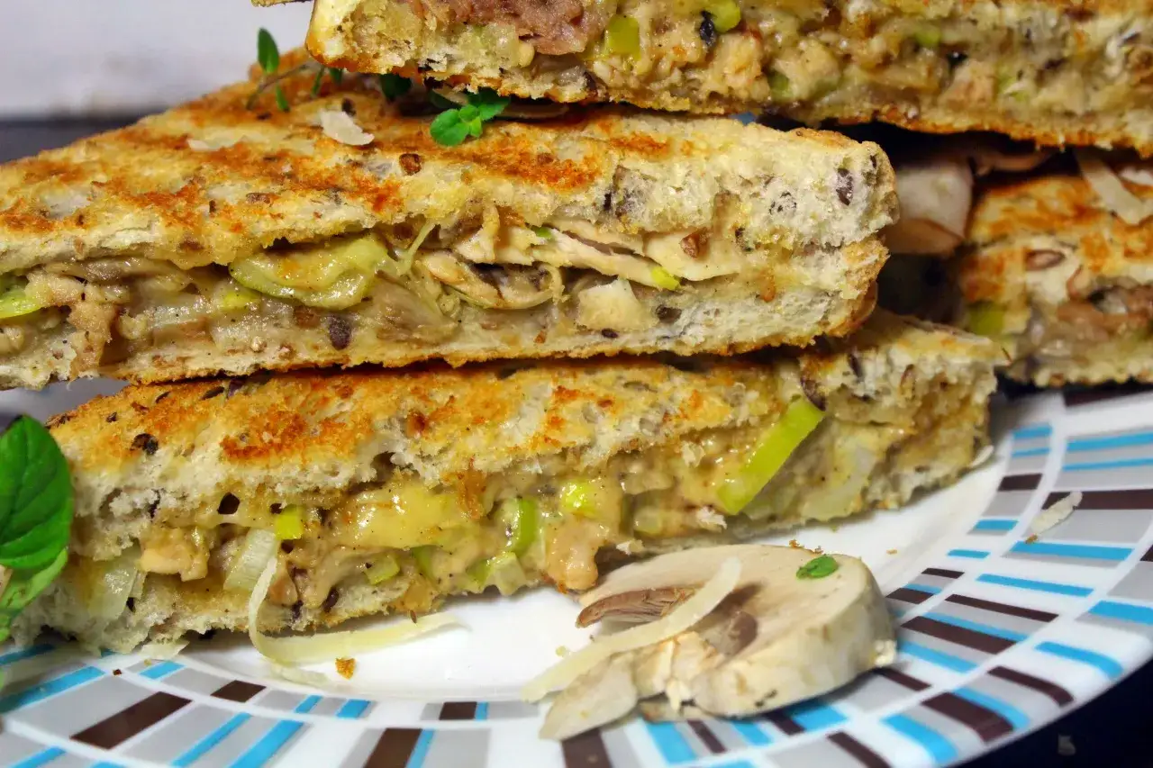 Pyszne tosty z pieczarkami, kurczakiem i serem, ułożone na talerzu w kratkę.