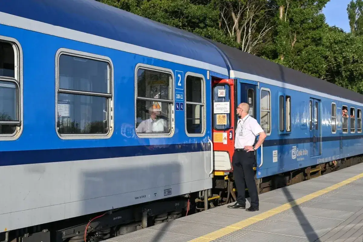 Konduktor w białej koszuli stoi przy drzwiach niebieskiego pociągu InterCity na peronie.