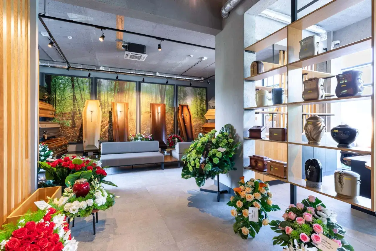 Wnętrze zakładu pogrzebowego z trumnami, urnami i wieńcami pogrzebowymi.