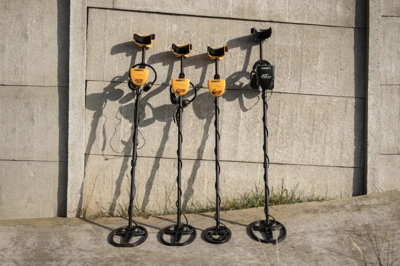 Cztery wykrywacze metali Garrett stojące pod betonową ścianą.