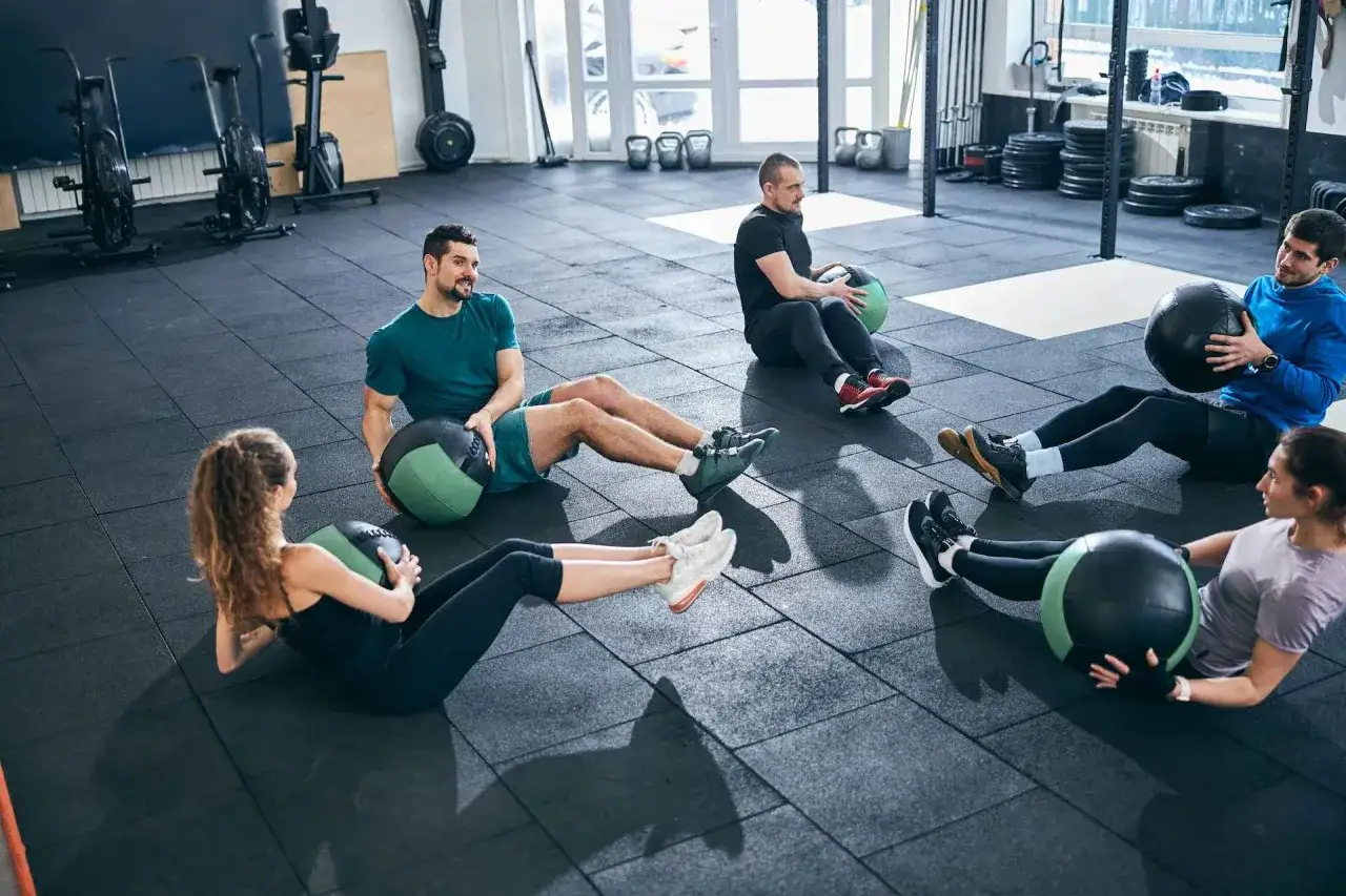 Fünf Personen machen im Fitnessstudio Sit-ups mit Medizinbällen.