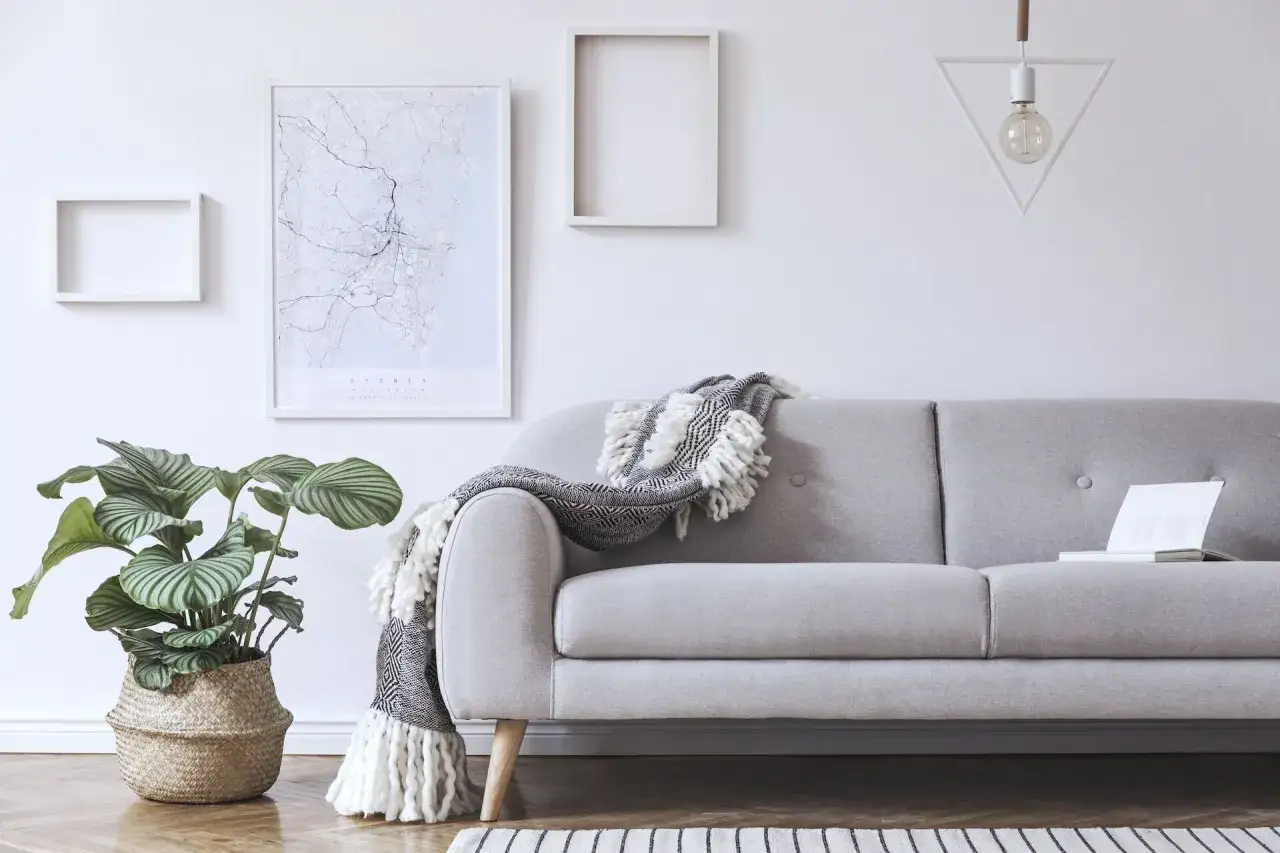 Przytulny salon z szarą kanapą, ozdobioną narzutą. Na ścianie mapa Sydney i geometryczna lampa.