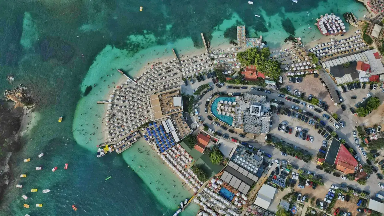 Albania najpiękniejsze miejsca: tętniący życiem kurort plażowy z białymi parasolami, turkusową wodą i basenami.