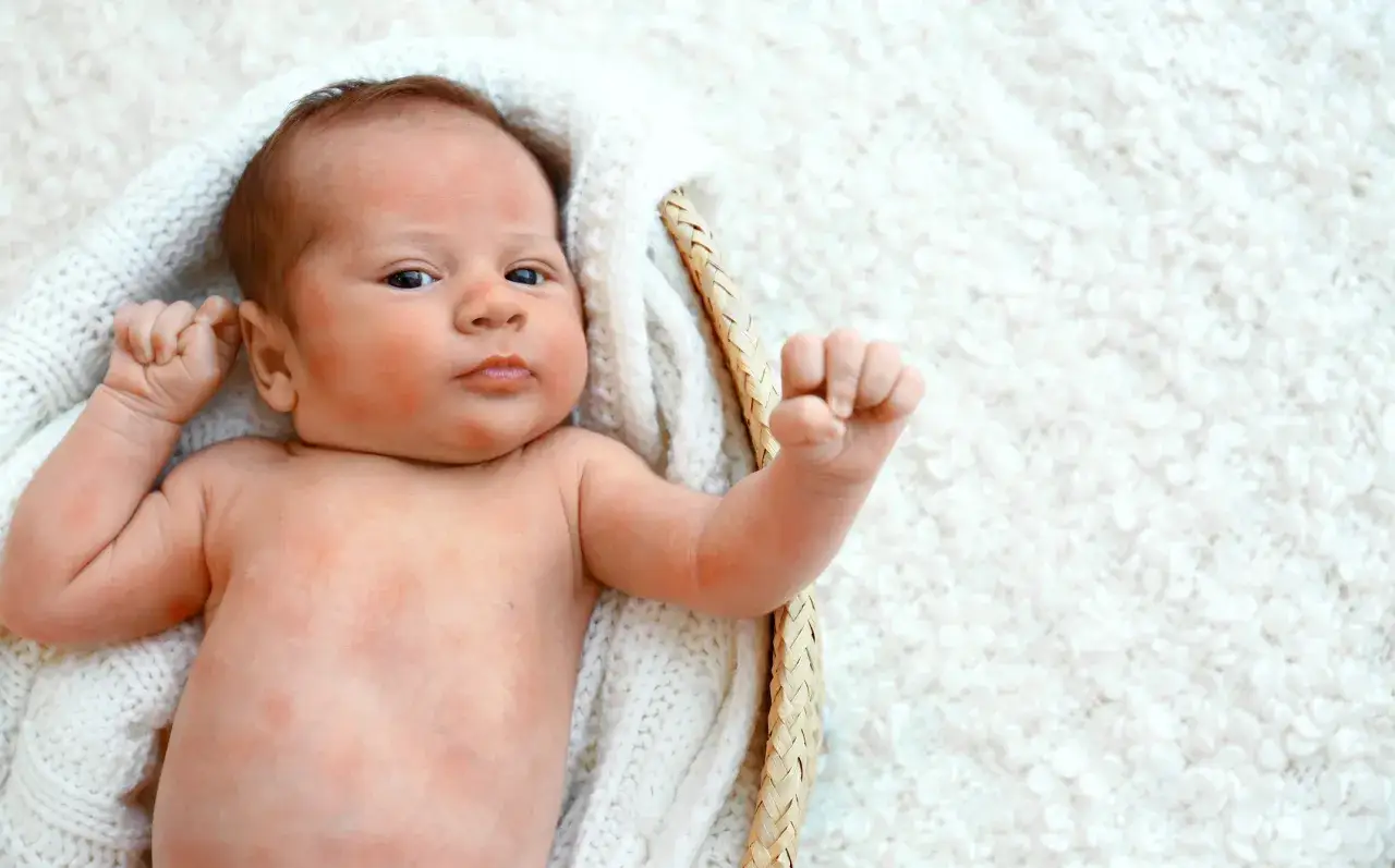 Noworodek w koszyku na białym kocyku, zaciśnięta piąstka.